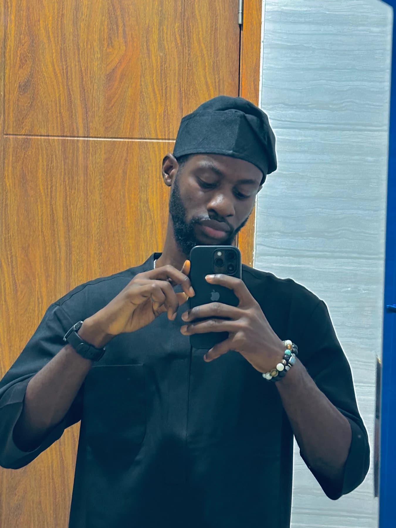 Bolade taking a mirror portrait, wearing a dark outfit and cap.