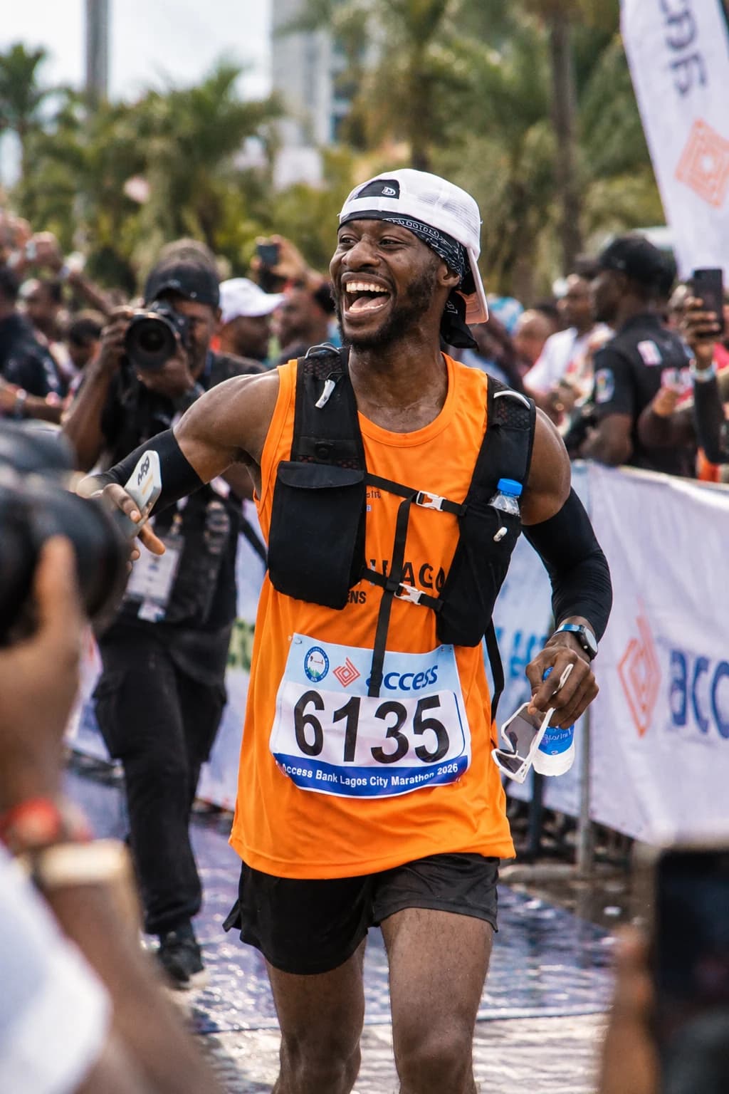 Bolade smiling at a marathon event in an orange running vest and race bib.