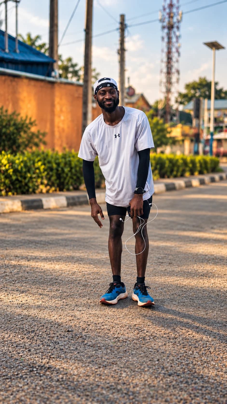 Bolade outdoors in a white running shirt and dark shorts, holding a phone and earphones.